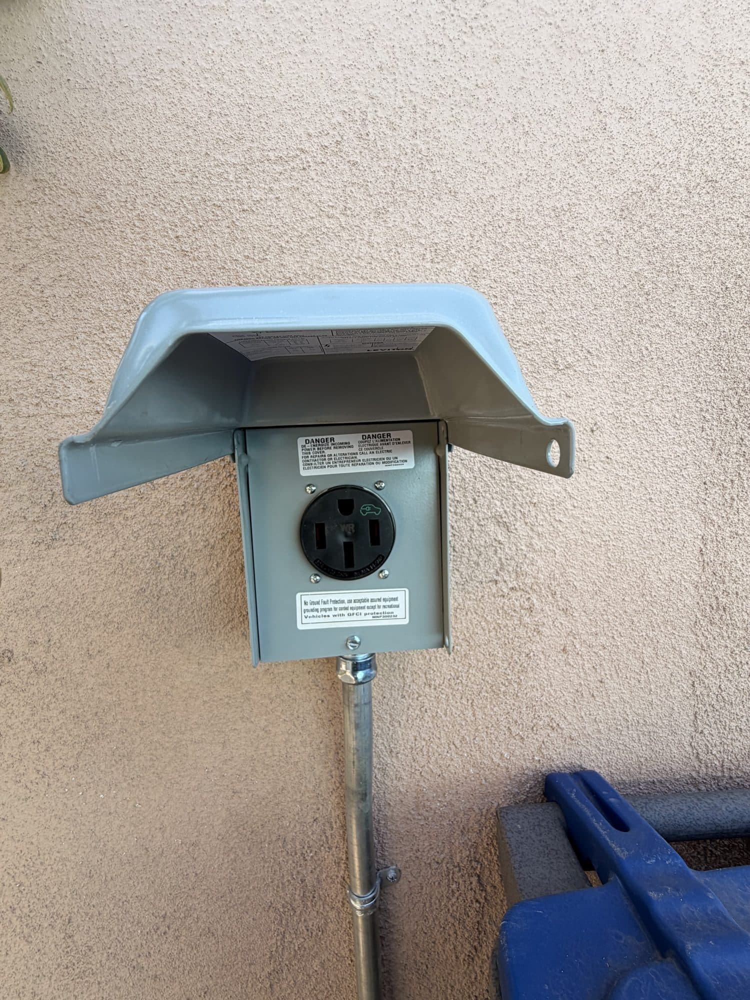 Outdoor 240-volt EV charging receptacle with weatherproof cover mounted on a stucco wall